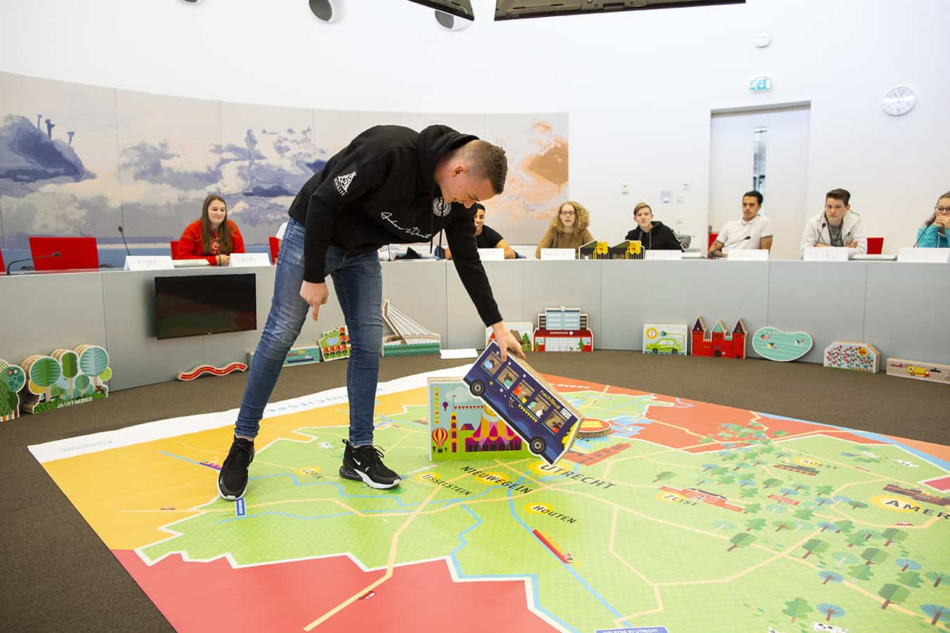 Jongen plaatst spelstuk nachtbus op de plattegrond van de provincie Utrecht tijdens het Provinciespel terwijl klasgenoten toekijken