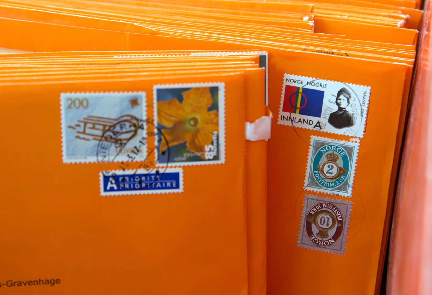 Op de afbeelding zijn oranje enveloppen te zien. Ze zijn verstuurd uit het buitenland, want je ziet bijvoorbeeld postzegels uit Noorwegen.